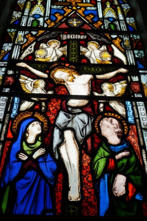 Stained glass with a man crucified, two angels, and two people crying at his feet.